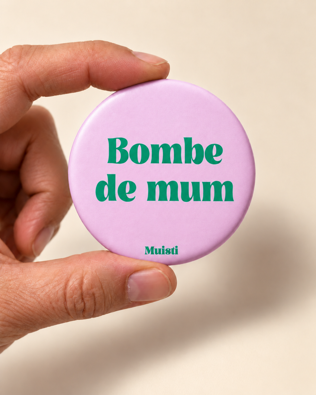 Magnet Muisti « Bombe de mum » tenu entre le pouce et l’index sur fond ivoire.