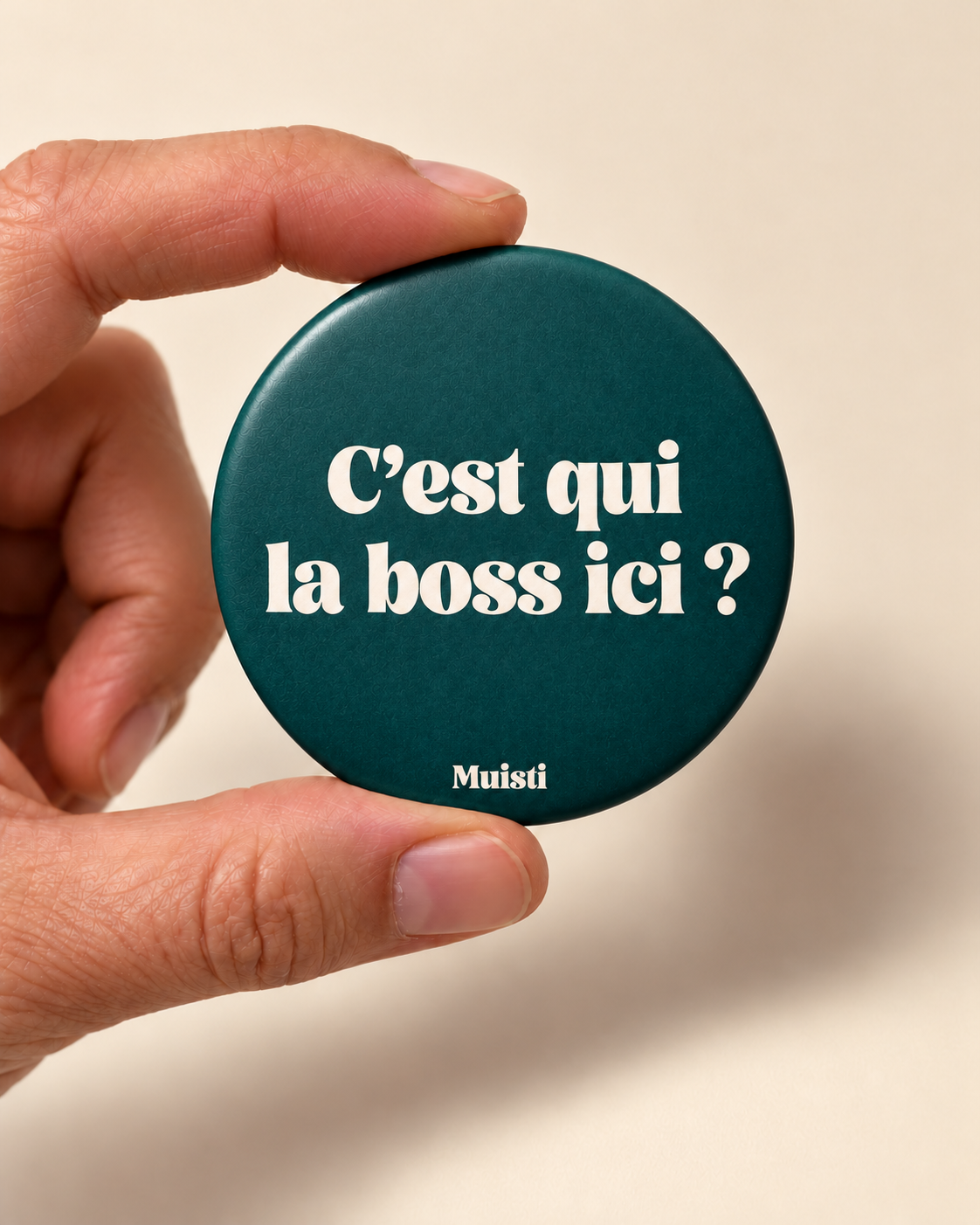Magnet Muisti « C’est qui la boss ici ? » tenu entre le pouce et l’index sur fond ivoire.