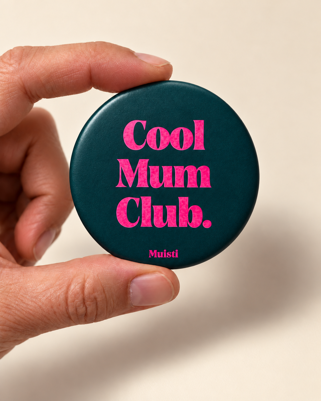 Magnet Muisti « Cool Mum Club » tenu entre le pouce et l’index sur fond ivoire.