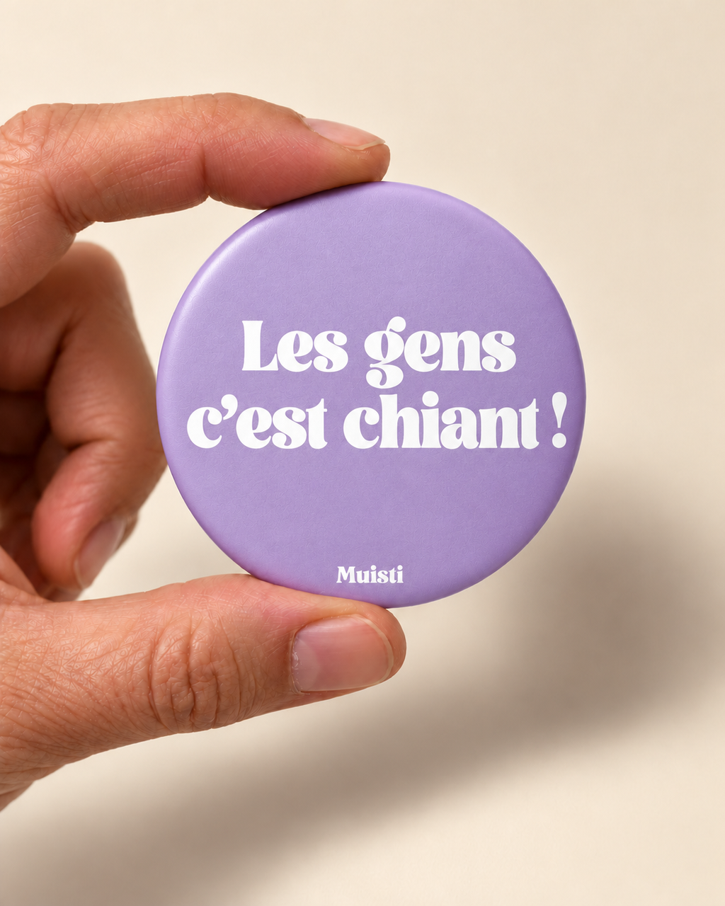Magnet Muisti « Les gens c’est chiant » tenu entre le pouce et l’index sur fond ivoire.
