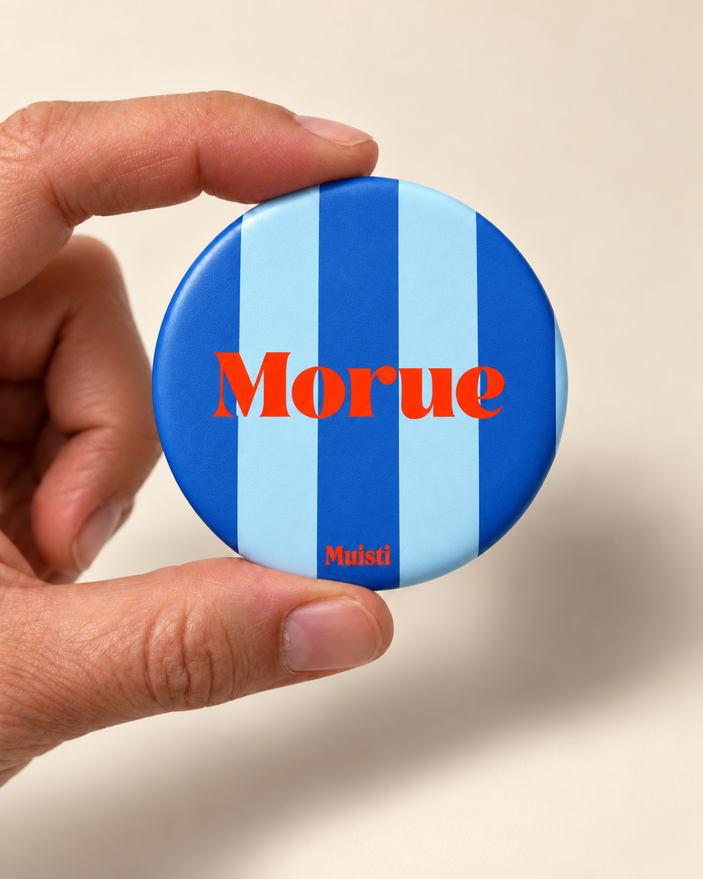 Magnet Muisti « Morue » tenu entre le pouce et l’index sur fond ivoire.