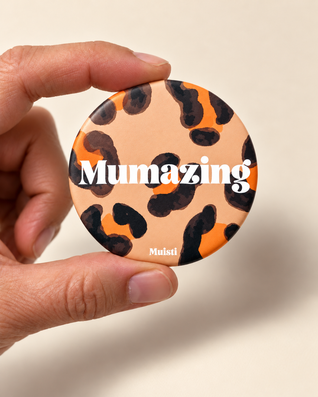 Magnet Muisti « Mumazing » tenu entre le pouce et l’index sur fond ivoire.