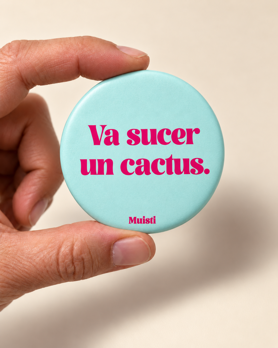 Magnet Muisti « Va sucer un cactus. » tenu entre le pouce et l’index sur fond ivoire.