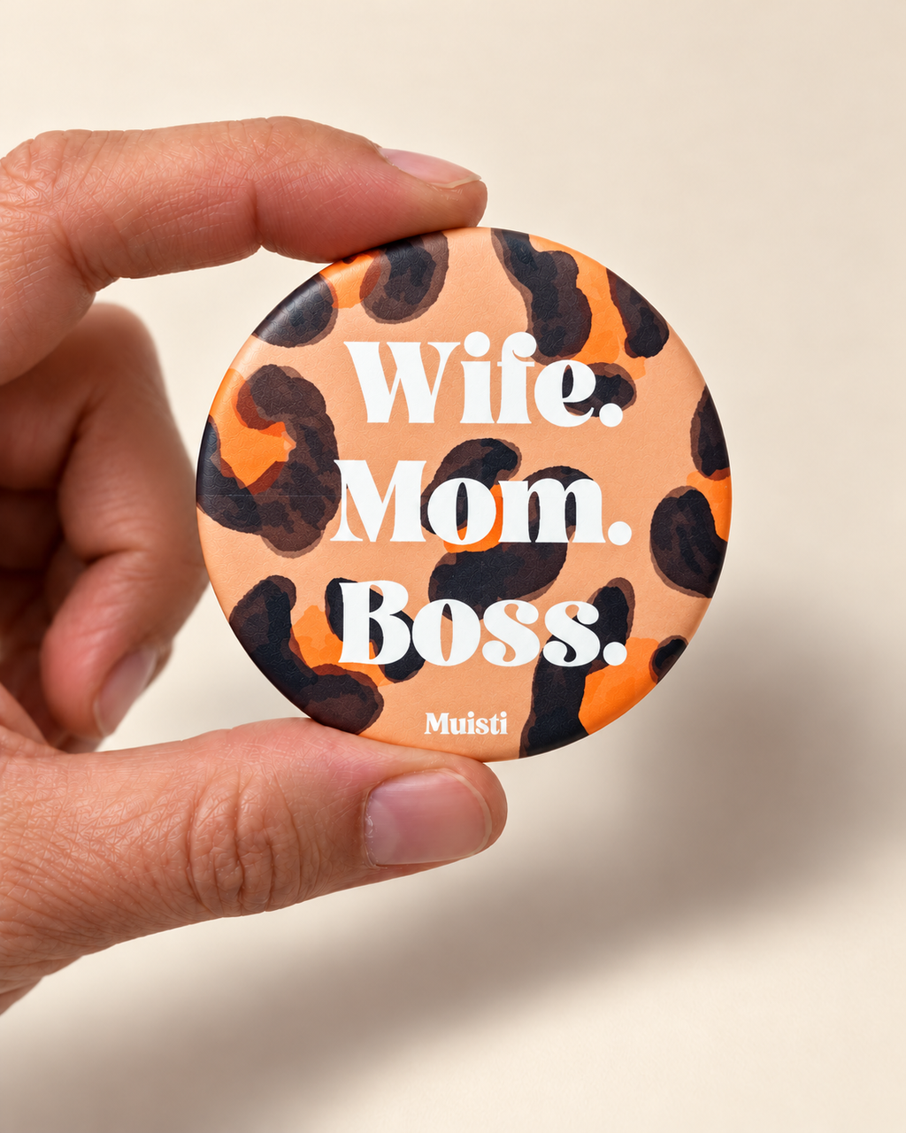 Magnet Muisti « Wife. Mom. Boss. » tenu entre le pouce et l’index sur fond ivoire.