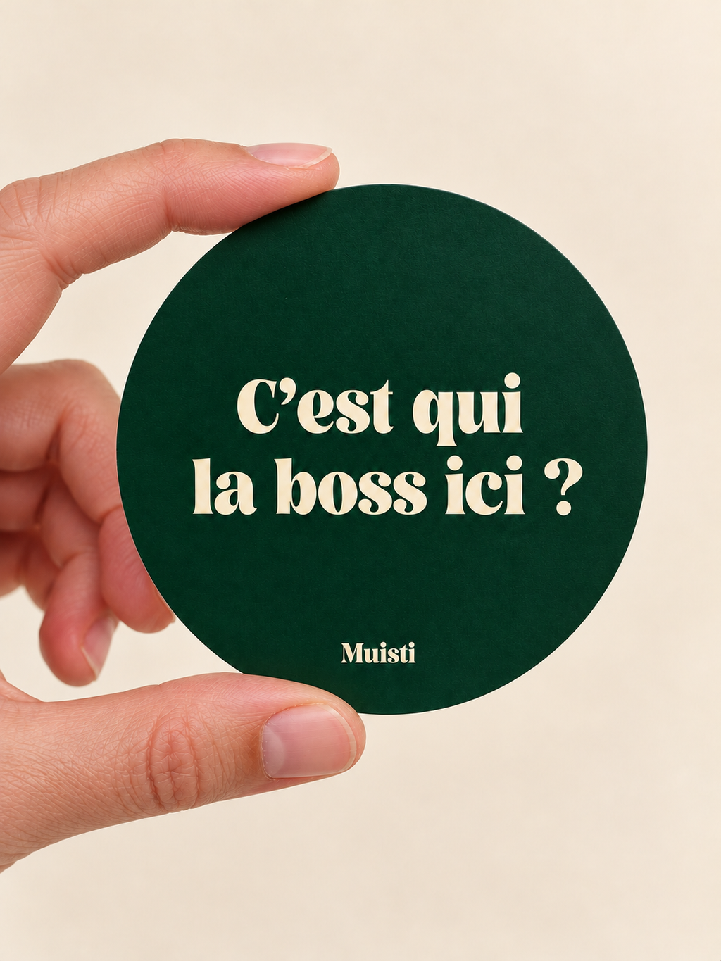 Sticker Muisti C’est qui la boss ici ? tenu entre le pouce et l’index sur fond ivoire