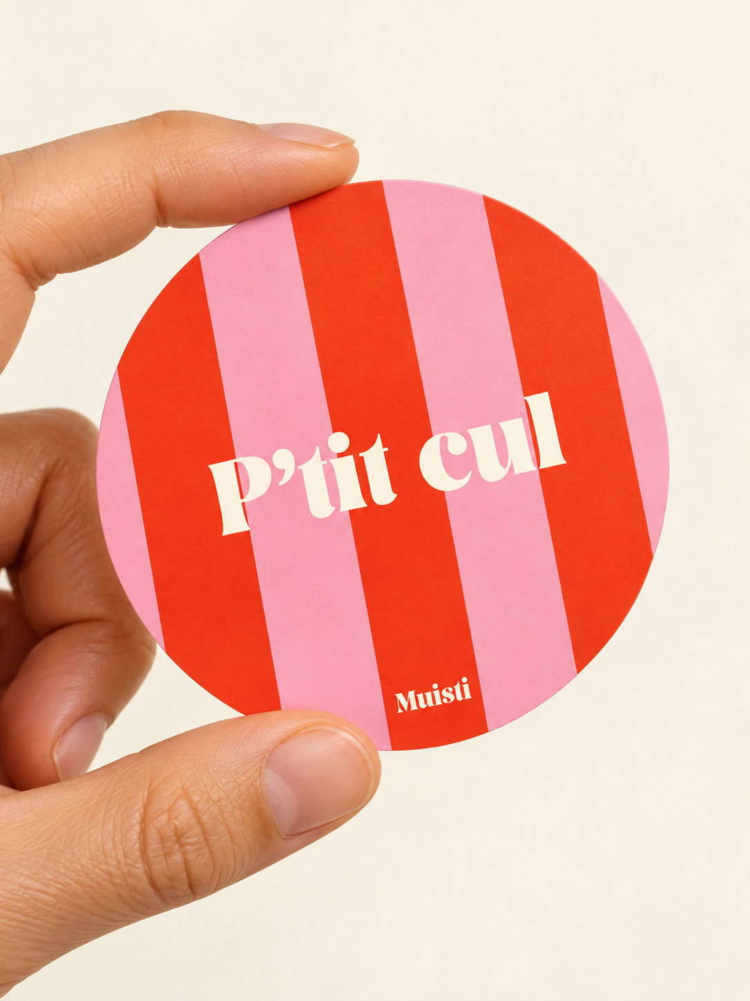 Sticker Muisti P’tit cul tenu entre le pouce et l’index sur fond ivoire