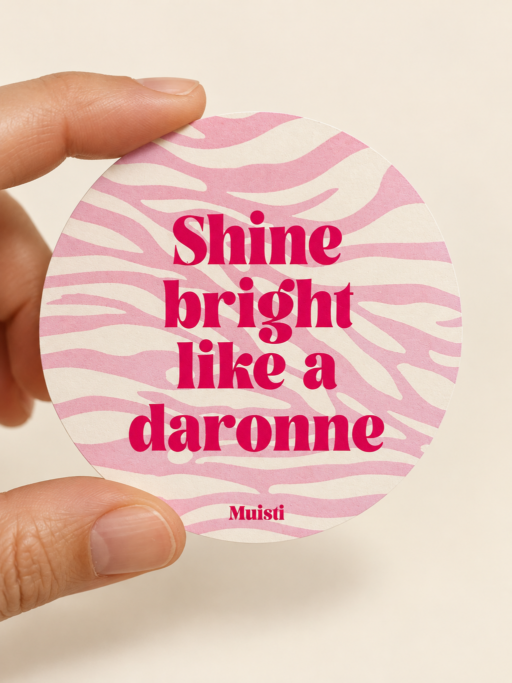 Sticker Muisti Shine bright like a daronne tenu entre le pouce et l’index sur fond ivoire