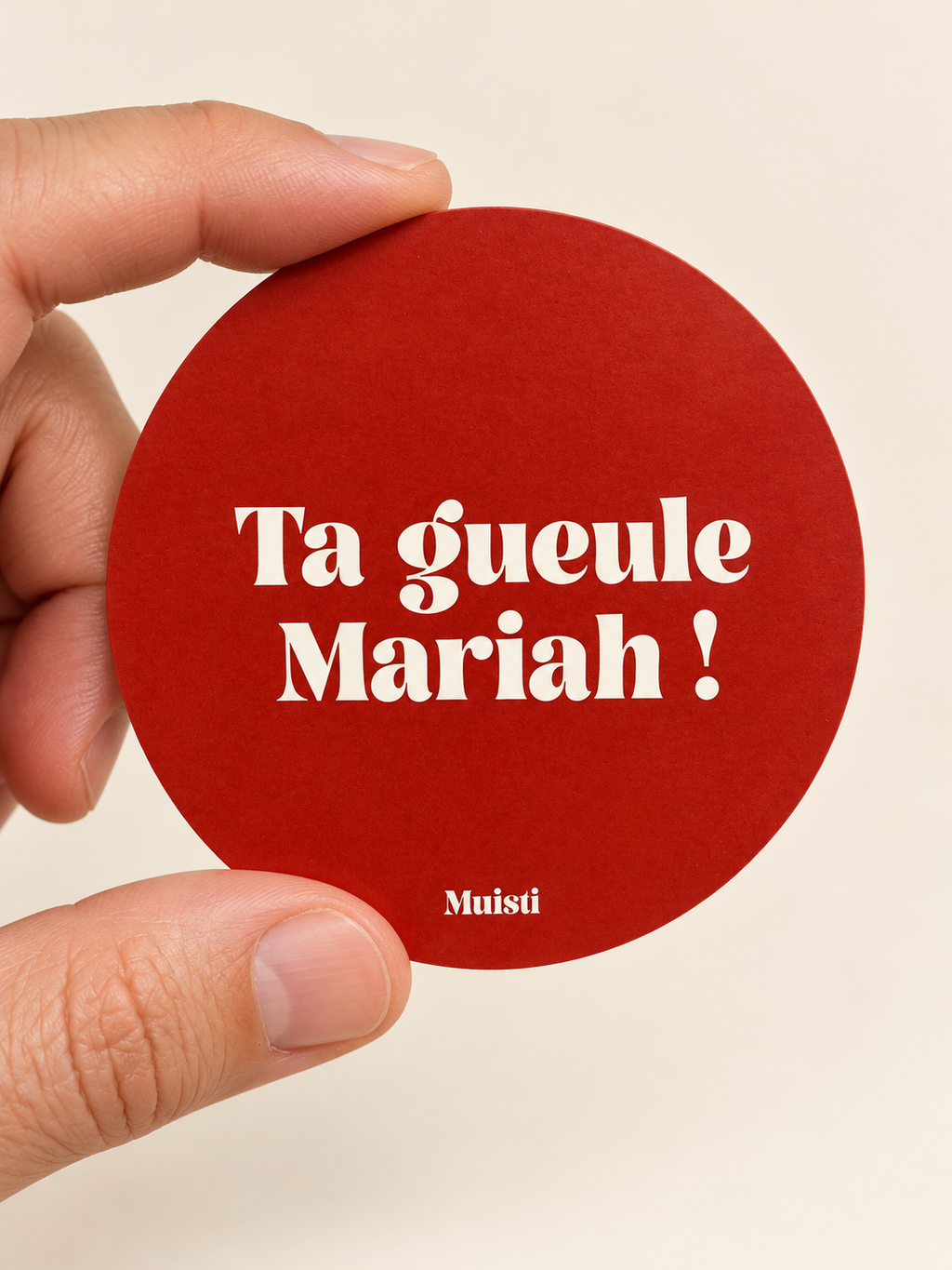 Sticker Muisti Ta gueule Mariah ! tenu entre le pouce et l’index sur fond ivoire